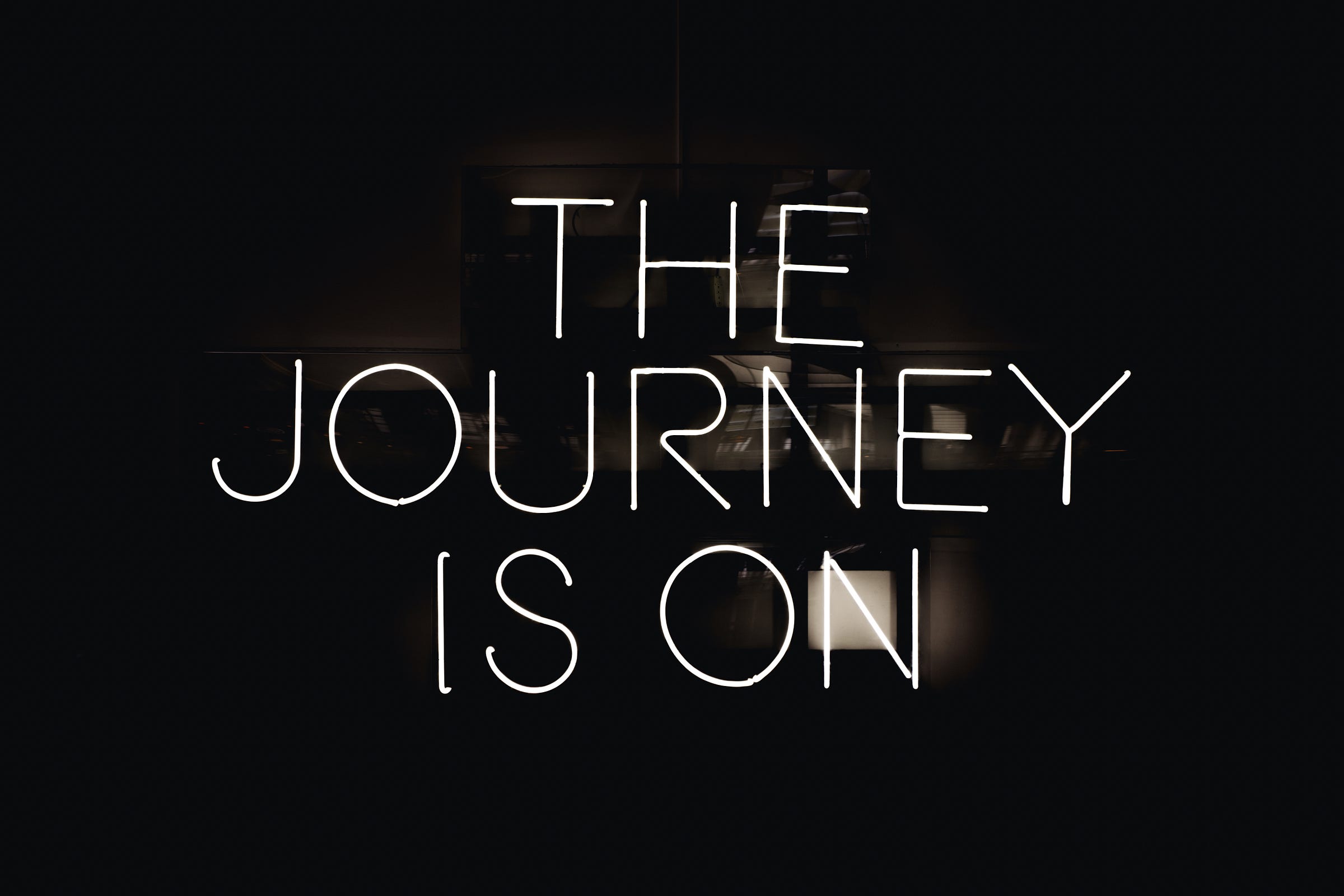 Neon sign reading "The journey is on" glowing in a dark room
