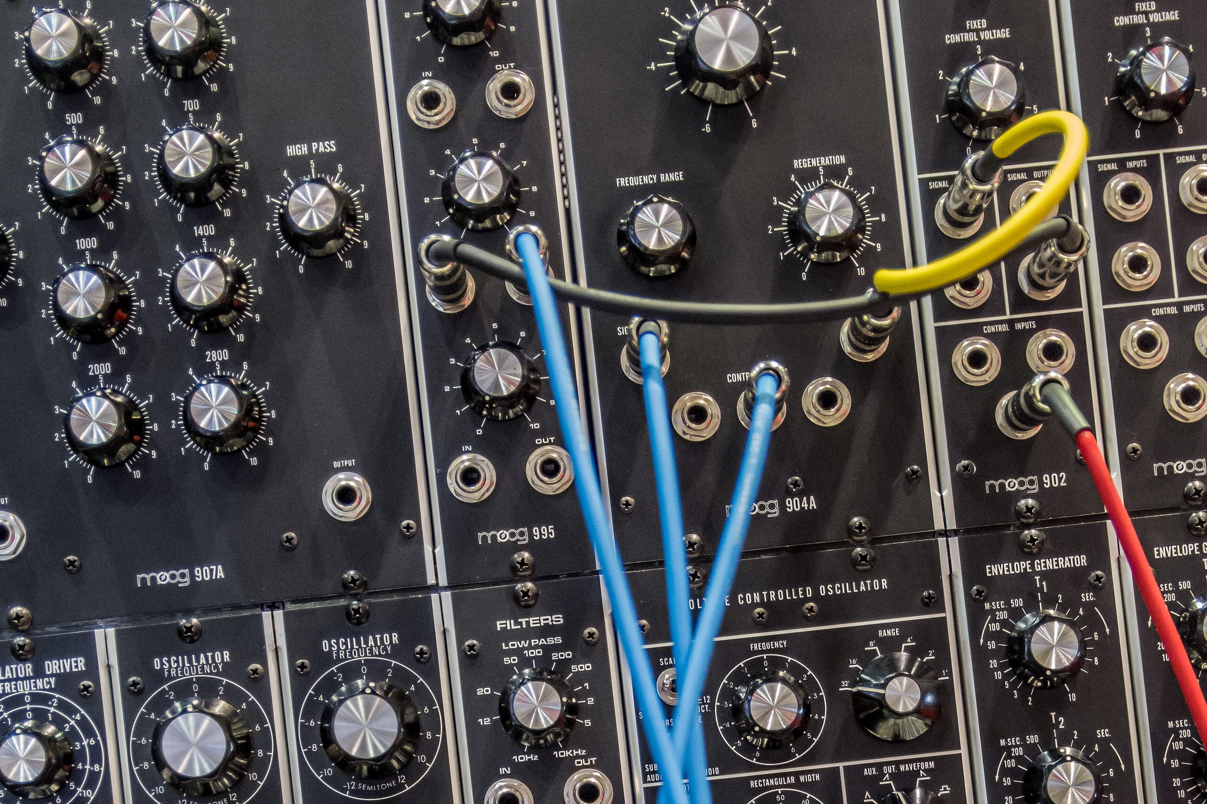 Close-up of a Moog modular synthesizer panel with rows of knobs, a low-pass filter section, and colorful patch cables